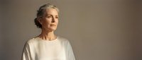 Mature Caucasian woman with gray hair in white sweater looking thoughtfully away against neutral background for lifestyle and aging concepts.