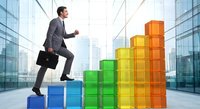 Professional businessman in gray suit climbing colorful block steps representing growth and success in modern corporate environment.