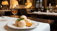 Elegant vanilla ice cream dessert with fresh mint and orange garnish served on white plate in upscale restaurant dining room with wine glass and ambient lighting.