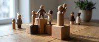 Wooden toy figures standing on blocks representing family hierarchy and social structure in warm natural lighting on wooden surface.