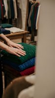 Woman hands touching stack of colorful knitted sweaters in walk-in closet. Cozy winter clothing organization and wardrobe storage concept.