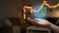 Digital security shield hologram floating above open palm with glowing protection symbol for cybersecurity and data safety concepts in modern office.