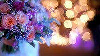 Pink roses and purple wildflowers bouquet against blurred golden bokeh lights background creates dreamy romantic atmosphere for wedding and celebration designs.