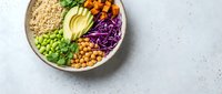 Colorful vegan Buddha bowl with quinoa, avocado, chickpeas, edamame, roasted sweet potato, and red cabbage on light background.