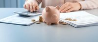 Young woman calculating personal finances with pink piggy bank and coins on desk surrounded by financial documents and paperwork for budgeting planning.