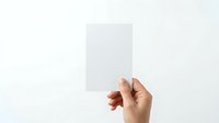 Hand holding blank white card or paper against neutral background for mockup, branding, advertising, or business presentation purposes.
