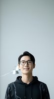 Young Asian male wearing black hoodie and eyeglasses, smiling against neutral white background. Portrait suitable for corporate profiles, tech industry, education, and professional networking materials.