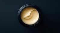 Luxurious golden face cream in black jar with smooth creamy texture for anti-aging skincare and beauty routine on dark background.