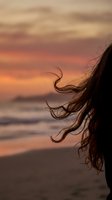 Woman with flowing hair silhouetted against golden sunset sky at ocean beach creating romantic atmospheric mood for wellness and freedom concepts.