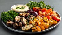 Grilled vegetables platter with mushrooms, colorful bell peppers, fresh herbs and creamy dip sauce served on gray ceramic plate. Mediterranean style appetizer.