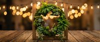 Festive green wreath with wooden star centerpiece on rustic table with warm bokeh lights creating cozy holiday atmosphere for seasonal decorating.