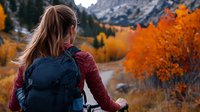 Young woman with backpack admiring vibrant autumn mountain landscape with golden aspen trees and rocky peaks during fall hiking adventure in wilderness.