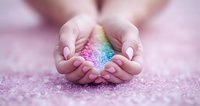 Female hands with manicured nails gently cupping colorful rainbow glitter against pink background, creating magical dreamy atmosphere. Concept of hope and wonder.