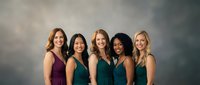 Five diverse professional women in elegant dresses standing together smiling, representing teamwork, friendship and business success in corporate environment.