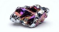 Iridescent bismuth crystal with rainbow metallic surface displaying purple, pink and gold colors on white background isolated for design projects.