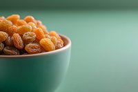 Golden raisins and dark sultanas in turquoise ceramic bowl against mint green background with copy space, selective focus for food packaging design.
