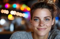 Young woman with freckles and natural smile against blurred colorful bokeh background. Casual gray sweater and messy updo hairstyle create authentic lifestyle portrait.