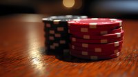 Stacked red and black poker chips on wooden table with dramatic lighting and shallow depth of field, creating atmosphere of casino gaming and gambling.