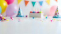 Colorful birthday party background with balloons, bunting flags and cake on white table. Festive celebration setup for children's party decorations.