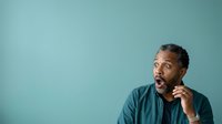 Middle-aged African American man with short gray hair wearing a teal button-up shirt, hand to chin, expressing surprise or thoughtful contemplation against solid blue background.