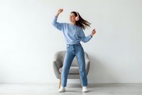 Young Asian woman dancing in casual blue outfit with headphones enjoying music at home on white background.