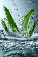 Fresh aloe vera leaves splashing in clear water with dynamic water drops and motion effect against gray background, natural skincare concept.