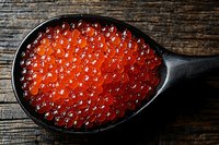 Fresh red caviar in black wooden spoon on rustic wooden background. Luxurious seafood delicacy with detailed texture of salmon roe pearls.