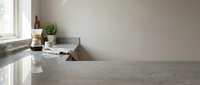 Modern minimalist kitchen interior with polished concrete countertops, white walls, natural light from window, and small potted herbs for contemporary home design.