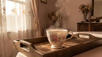 Vintage floral teacup on rustic wooden tray in cozy sunlit room with dried flowers and warm home decor creating peaceful morning atmosphere.