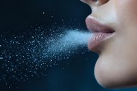 Close up of feminine lips exhaling frozen breath with sparkling particles against dark background, creating magical atmospheric effect in cold winter air.