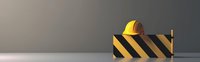 Yellow construction hard hat on black and yellow striped barrier against gray background, minimalist industrial safety concept with copy space.