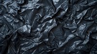 Dark crumpled metallic fabric texture with dramatic shadows and highlights creates an abstract luxury background perfect for modern design projects and premium presentations.