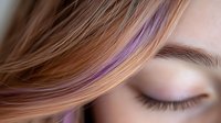Close up view of closed eye with long eyelashes and brown hair with purple highlight streak falling across face, showing natural beauty and peaceful expression.
