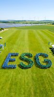 Aerial view of people forming ESG letters on green field with wind turbines and solar panels showcasing environmental social governance sustainability concept.