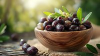 Fresh black olives with green leaves in wooden bowl on rustic background, natural light setting creates appetizing Mediterranean mood.
