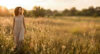 Young woman in white dress standing in golden wheat field during sunset with warm light creating peaceful rural atmosphere for lifestyle content.
