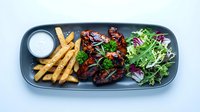 Grilled meat with herbs served on dark plate alongside golden fries and fresh mixed greens salad with white sauce for restaurant dining experience.