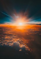 Dramatic aerial view of sunset above fluffy clouds with orange and teal sky, sunburst breaking through cloudscape creating ethereal atmosphere for backgrounds.