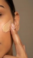 Young woman applying liquid foundation makeup with finger on face showing skincare routine and cosmetic application technique for flawless complexion.