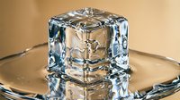 Crystal clear ice cube melting on transparent glass plate with water droplets and reflections for beverage photography and cooling concepts.