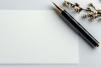 Elegant black fountain pen with gold accents next to blank white paper and delicate dried flowers, creating minimalist composition for business or writing concept.