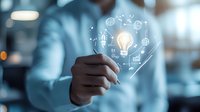 Professional holding glowing light bulb with digital business icons floating around in modern office environment. Innovation concept for business solutions.
