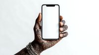 African American hand with tattoos and silver bracelets holding modern smartphone with blank white screen against neutral background.
