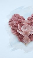 Delicate pink carnation petals arranged in heart shape on soft watercolor background for romantic wedding and love concepts.