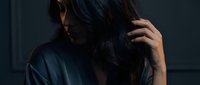 Young Asian woman with long dark hair touching head in moody lighting, expressing stress, headache or mental health concerns in dramatic indoor setting.