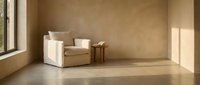 Minimalist interior with beige armchair, wooden side table, and natural light from large window in empty room.