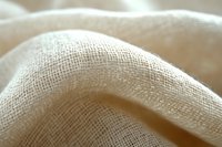 Natural linen fabric close-up showing detailed texture and weave pattern in soft beige tones with gentle folds and curves creating an organic abstract composition.