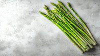 Fresh green asparagus spears arranged on textured gray concrete background, raw organic vegetables for healthy cooking.