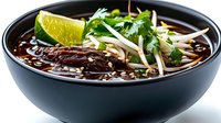 Asian beef noodle soup with fresh herbs, lime wedge and bean sprouts in dark bowl isolated on white background ready for culinary design projects.