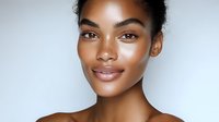Young African American woman with glowing natural makeup and radiant skin smiling confidently against light background, showcasing fresh, dewy complexion and flawless beauty look.